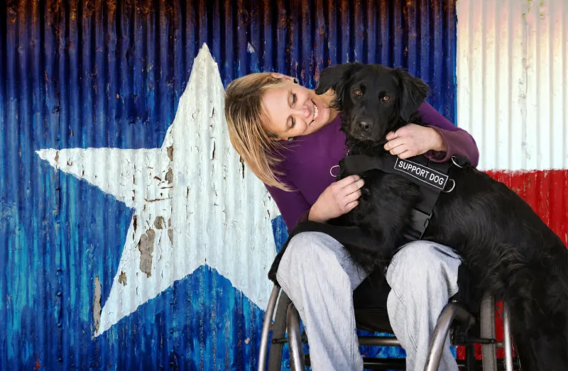 A person with a disability and a support dog against a Texas flag.